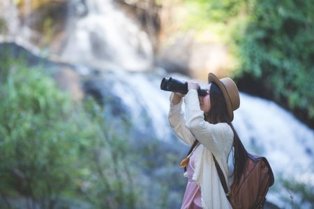 Female tourist who is looking at the binoculars to see the atmosphere at the waterfall